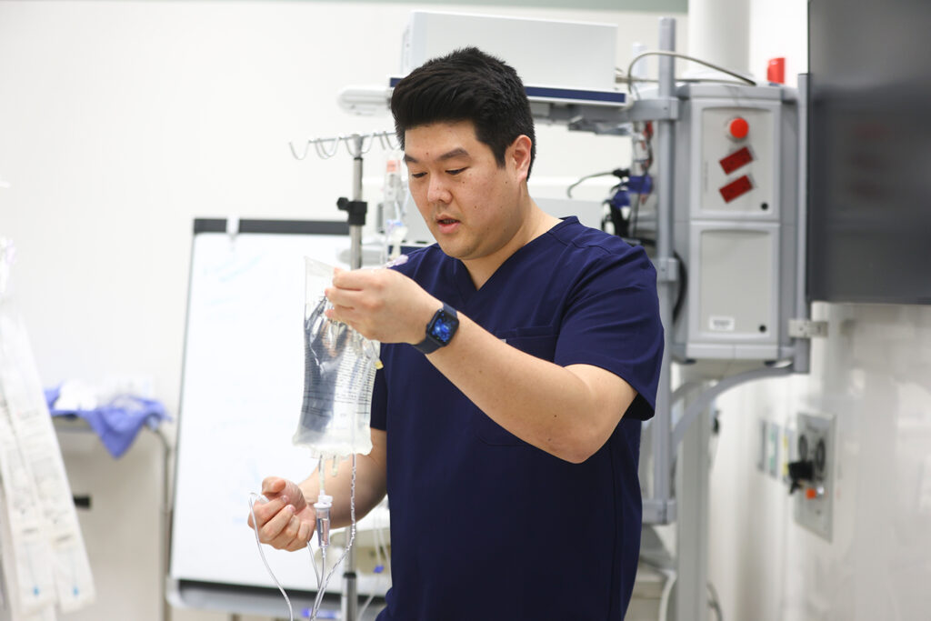 A candid image of pharmacist Alex Kim preparing an IV bag that contains a clear fluid.