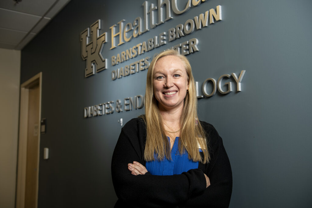 Kristina NasemanReynolds smiling standing in front of a will wiht the hospital name.